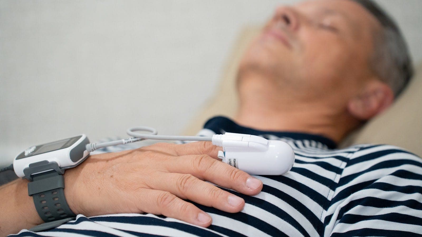Naprava WatchPAT — senzorja na zapestju in prstu med nočnim testiranjem doma